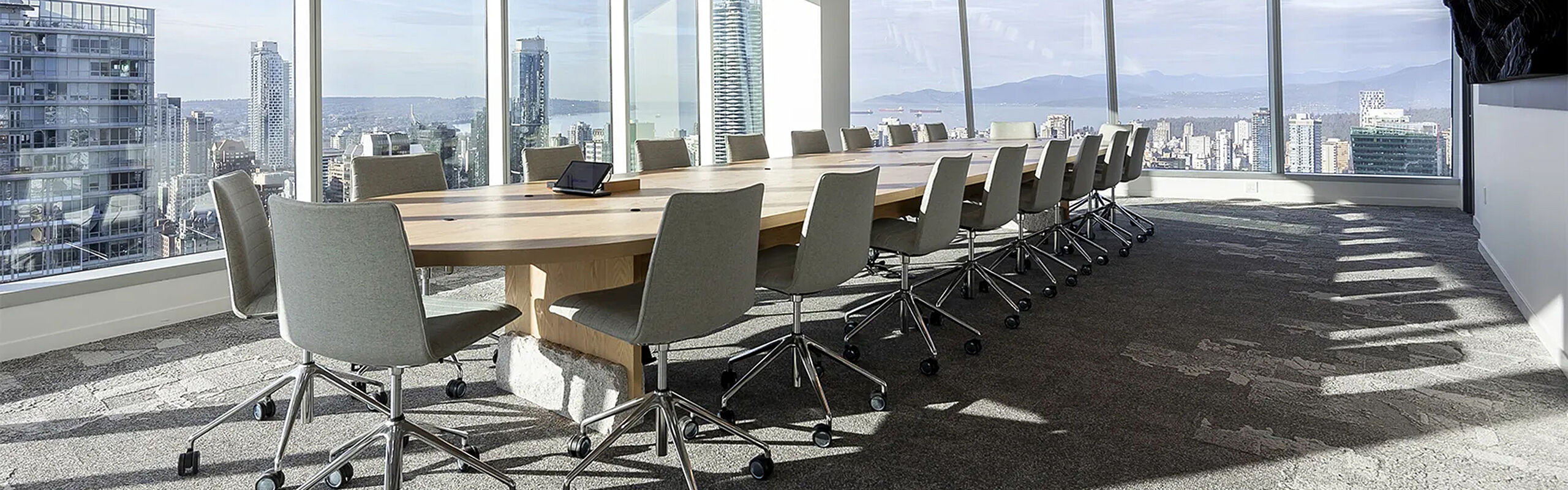 Moderner Konferenzraum mit großem Besprechungstisch, ergonomischen Bürostühlen und bodentiefen Fenstern mit Blick über eine Stadt – Beispiel für hochwertig gestaltete Büroarbeitswelt.