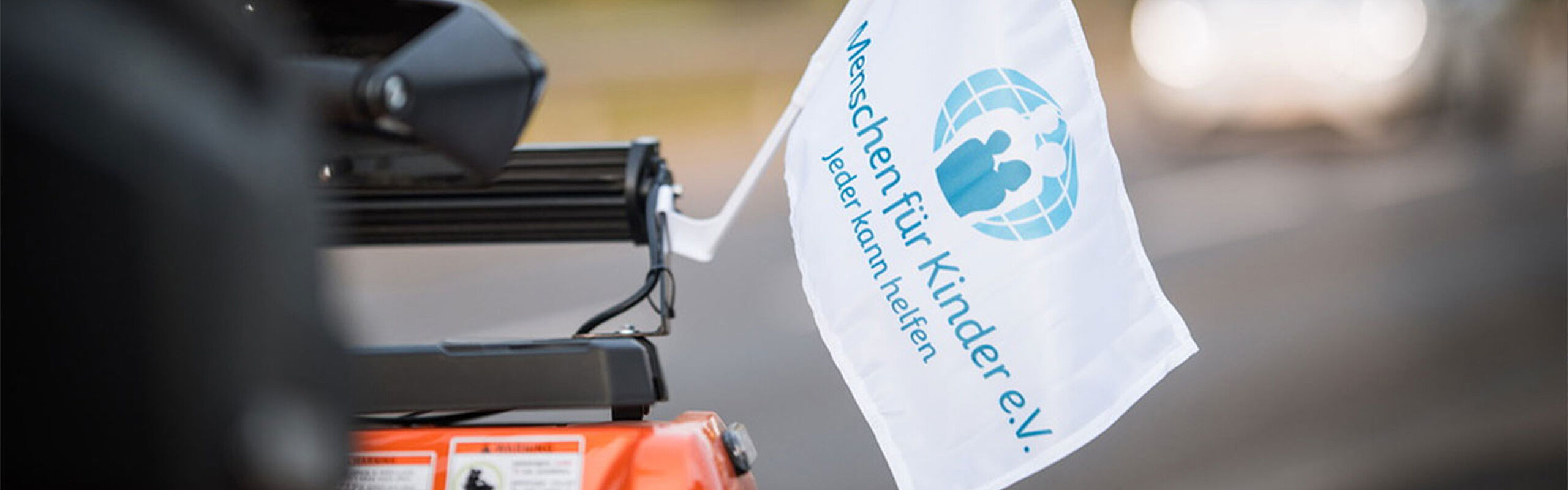Wehende weiße Flagge mit blauem Menschen für Kinder e.V. Logo befestigt an einem Quad