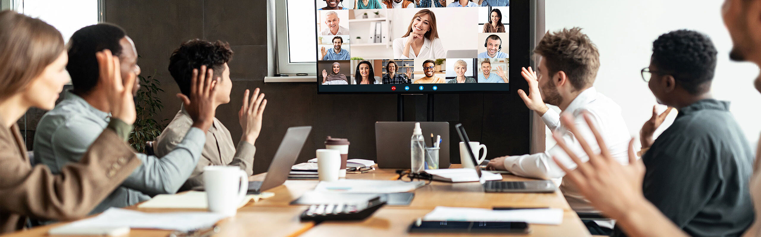 Menschen im Konferenzraum winken in Kamera von Videokonferenz