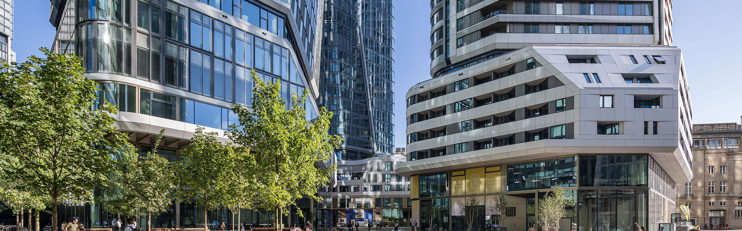 Außenansicht des Gebäudekomplexes FOUR Frankfurt mit Hochhaustürmen und begrüntem Vorplatz
