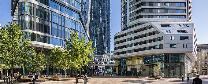 Außenansicht des Gebäudekomplexes FOUR Frankfurt mit Hochhaustürmen und begrüntem Vorplatz