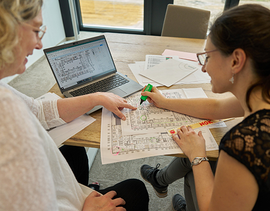 Zwei Personen arbeiten gemeinsam an Grundrissen und Plänen – kollaborative Ausführungsplanung in der Entwicklung moderner Arbeitswelten.