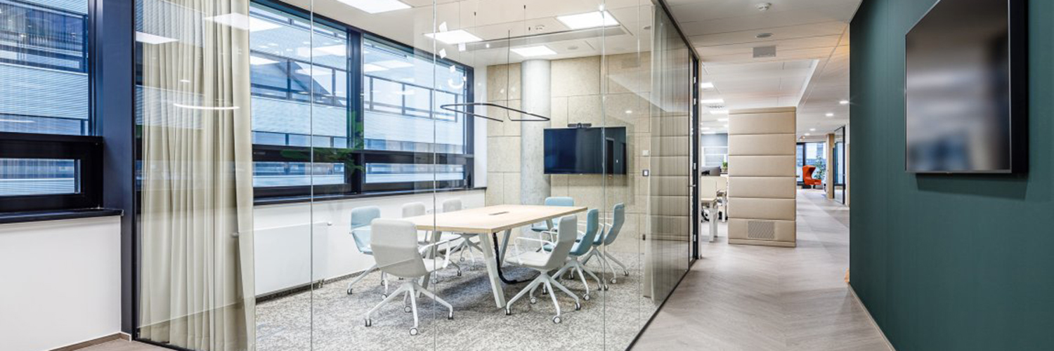 Moderner Besprechungsraum mit Glastrennwänden, Konferenztisch und ergonomischen Stühlen, integriert in eine helle Bürofläche mit Flur und Arbeitsbereichen.