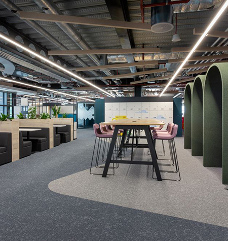 Modernes Büro mit offenen Arbeits- und Begegnungsbereichen, Hochtisch mit Barhockern, Sitznischen und Akustik-Elementen, kombiniert mit industrieller Decke und integrierter Beleuchtung.