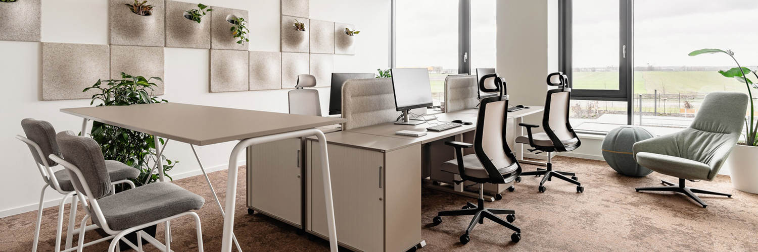 Moderne Arbeitsumgebung mit ergonomischen Arbeitsplätzen, informellem Besprechungsbereich und biophilen Gestaltungselementen. Die Kombination aus Tageslicht, Akustiklösungen und unterschiedlichen Arbeitszonen unterstützt konzentriertes Arbeiten, Kommunikation und Wohlbefinden.