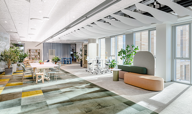 Heller, offener Bürobereich mit flexiblen Arbeitszonen, Sitzbereichen, Pflanzen und großen Fensterflächen mit viel Tageslicht