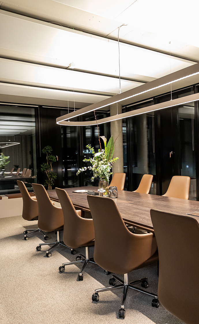 Elegant conference room with a large meeting table, leather chairs and modern ring lighting in front of dark glass panels.