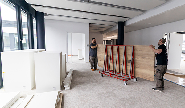 Zwei Personen tragen eine Tischplatte in einer Baustelle