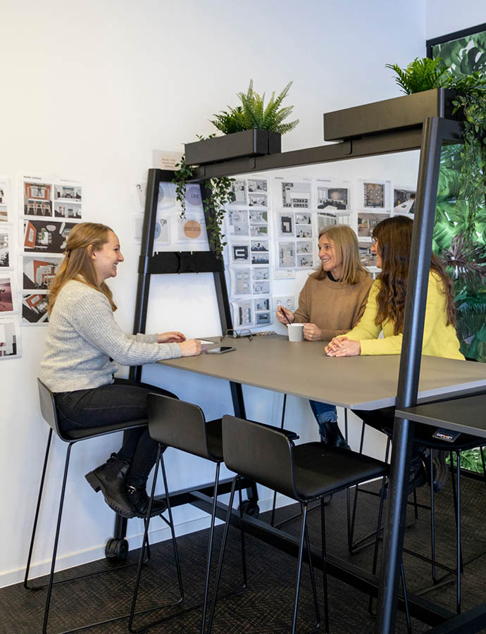 Drei Personen sitzen an einem Hochtisch und unterhalten sich