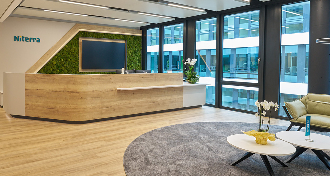 Empfangstheke aus Holz mit Wandbildschirm große Fensterfront und Wartebereich mit Loungeecke