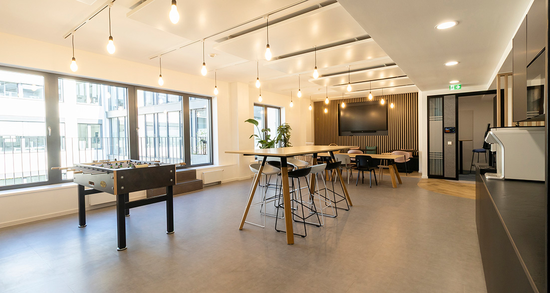 Workcafe mit Kicker Tisch und Sitzbänken und Küche rechts im Bild