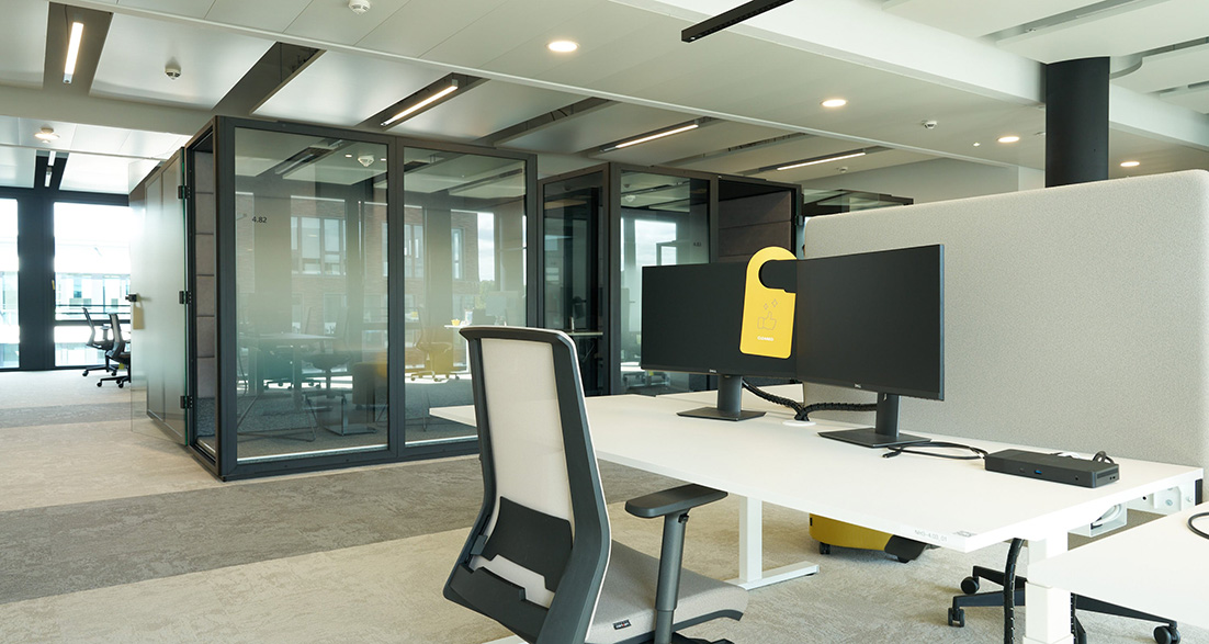 Bildschirmarbeitsplatz mit Bürostuhl und Akustikboxen im Hintegrund