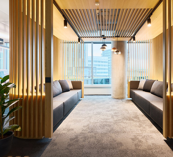 Modern office corridor with wooden slats, integrated seating niches, and warm lighting for informal meetings.