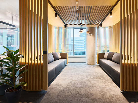 Modern office corridor with wooden slats, integrated seating niches, and warm lighting for informal meetings.