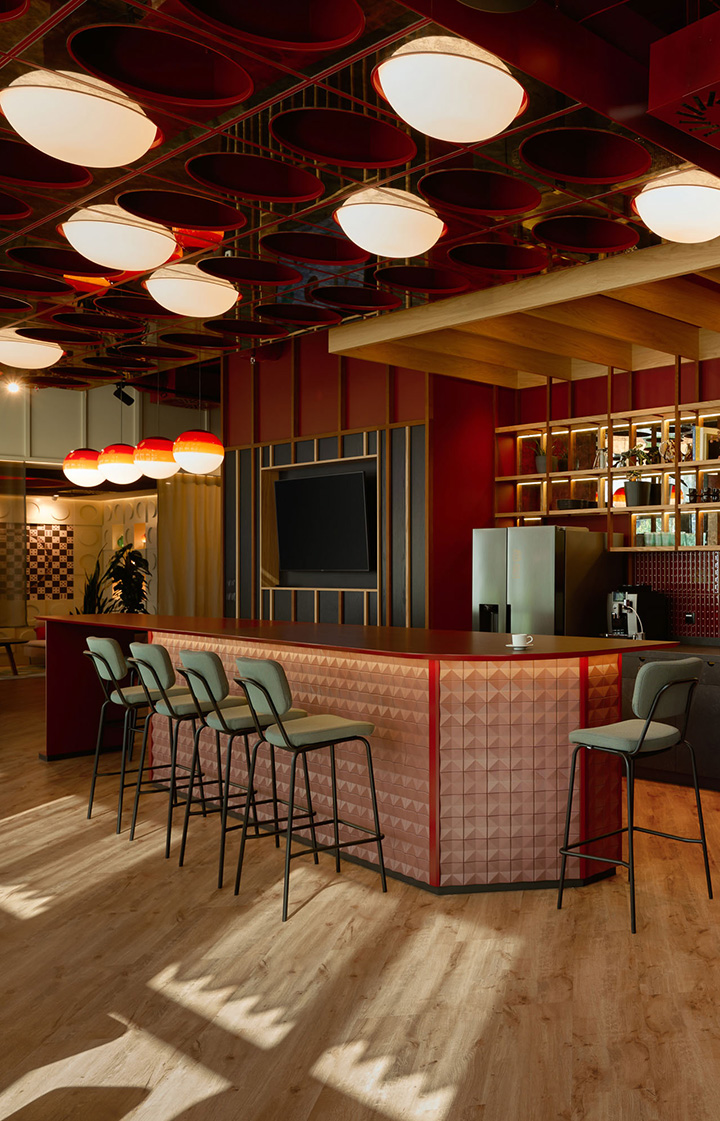 Designorientierter Bar- und Aufenthaltsbereich mit markanter roter Decke, runden Leuchtelementen und Tresen mit Barhockern in moderner Büroumgebung.