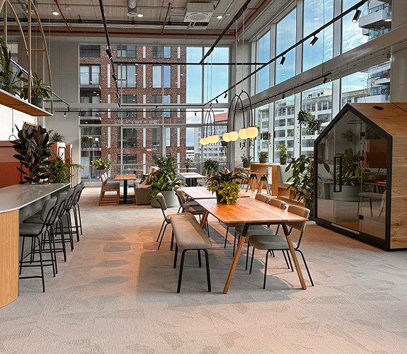 Heller Aufenthaltsbereich mit großen Fensterflächen, Holzmöbeln und offenen Sitzbereichen für Austausch und Zusammenarbeit.