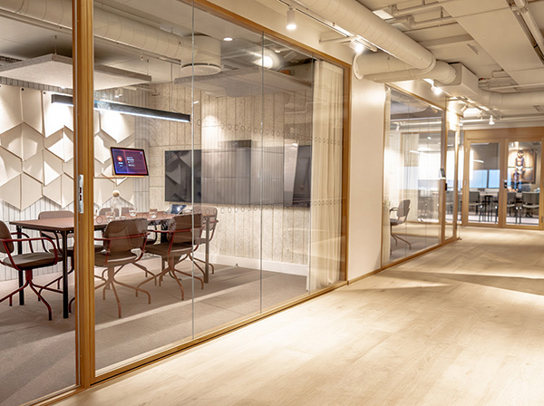 Transparente Besprechungsräume mit Glaswänden, warmen Holzdetails und Blick in eine offene Bürostruktur.