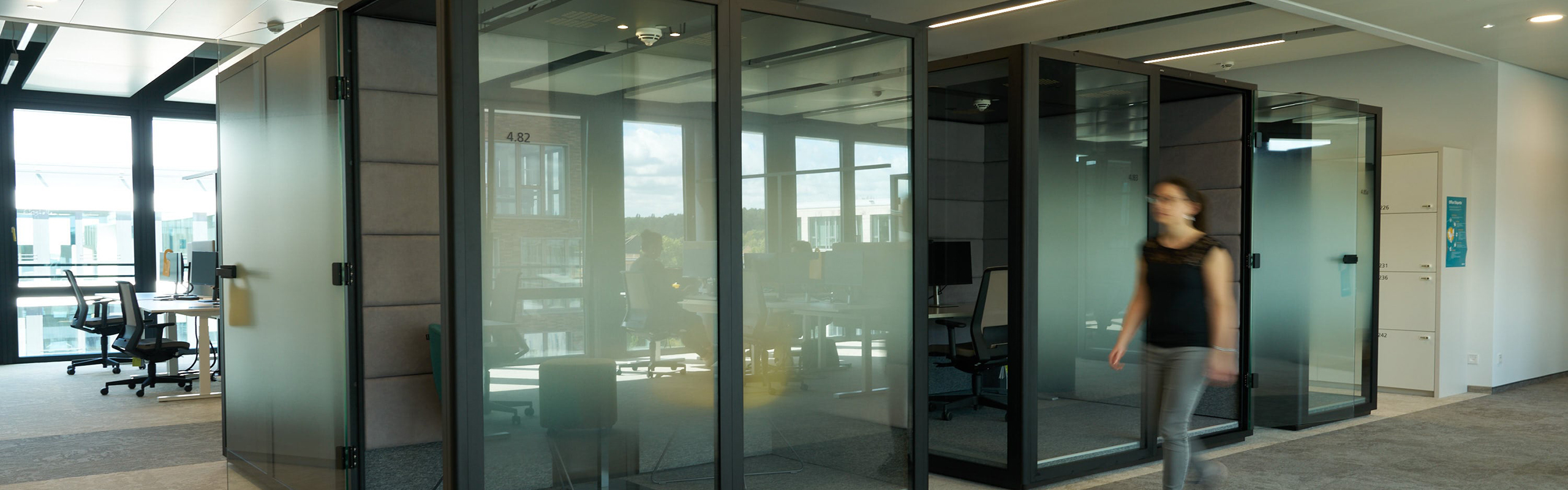 Eine Person läuft an einer Reihe von Akustikboxen im Büro vorbei