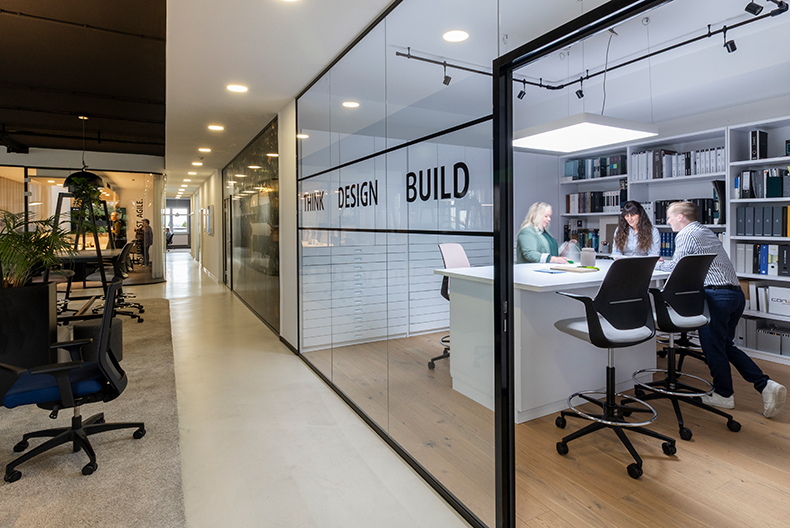 Modernes Büro mit Meetingraum aus Glas Drei Personen stehen an einem Hochtisch und arbeiten zusammen