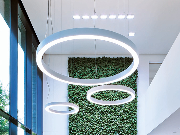 Moderne Ringleuchten an hoher Decke mit Mooswand im Hintergrund