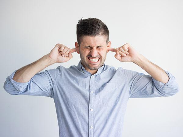 Mann hält sich die Ohren zu Lärm im Büro