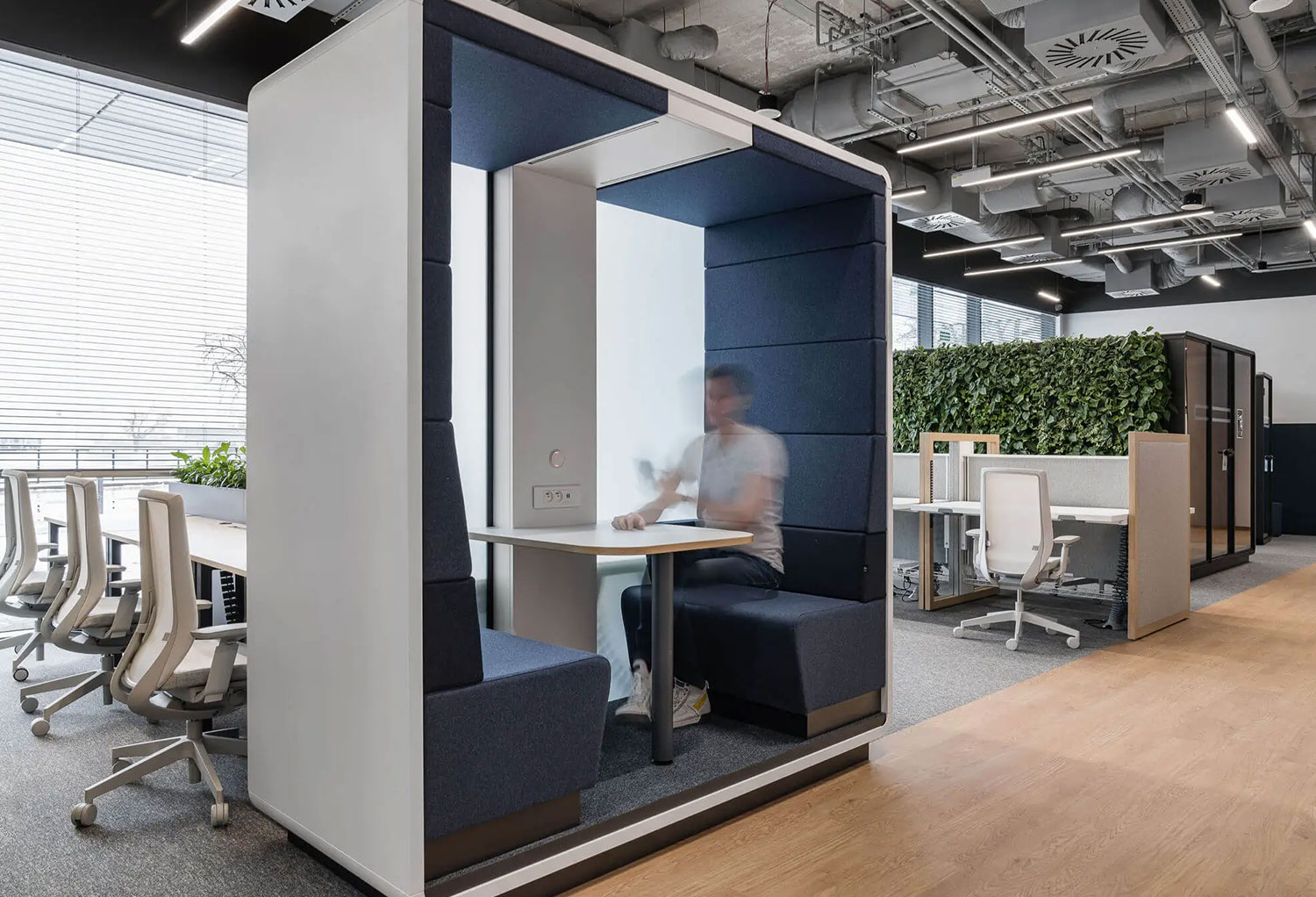 Arbeitender Mann in Akustikbox in Großraumbüro