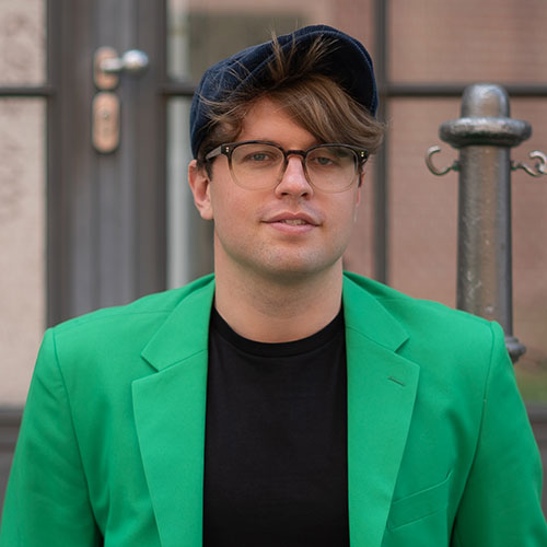 Junger Mann in einem grünem Anzug mit Baskenmütze und Brille