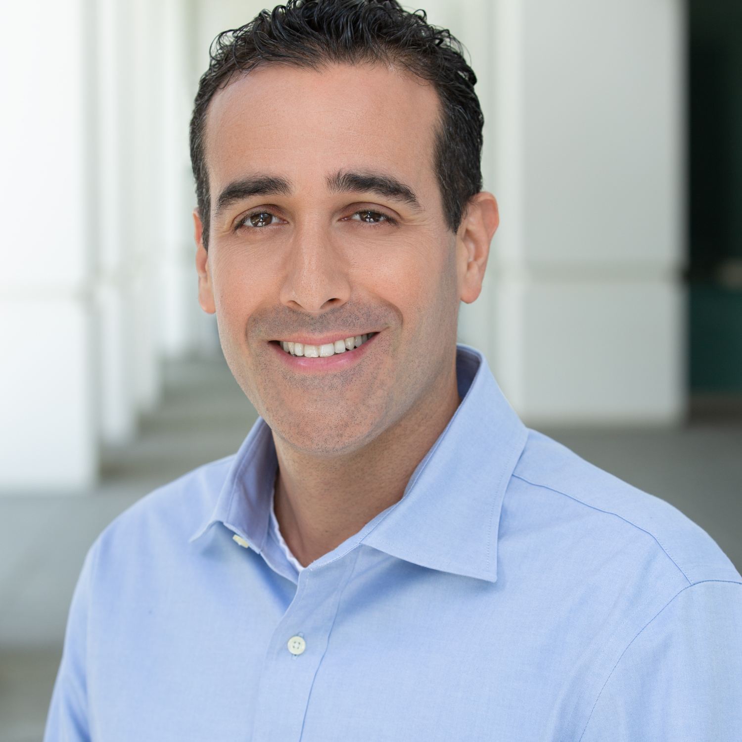 Ein lächelnder Mann mit dunklem Haar und hellblauen Hemd