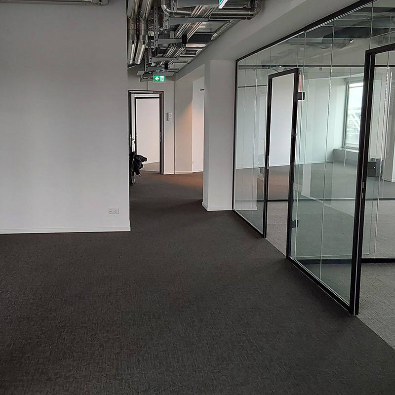 Flur- und Erschließungsbereich im Büro mit Glaswänden, Teppichboden und sichtbarer Gebäudetechnik.