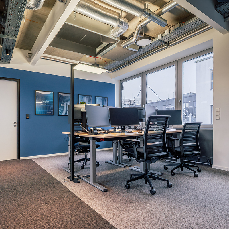 Fertiggestellter Büroarbeitsbereich mit Teamarbeitsplätzen, Monitoren, ergonomischen Stühlen und Tageslicht.