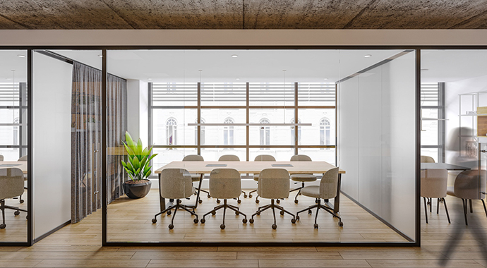 Heller Besprechungsraum hinter Glas mit großem Tisch, Drehstühlen und Pflanze vor bodentiefen Fenstern in einer modernen Bürogestaltung.