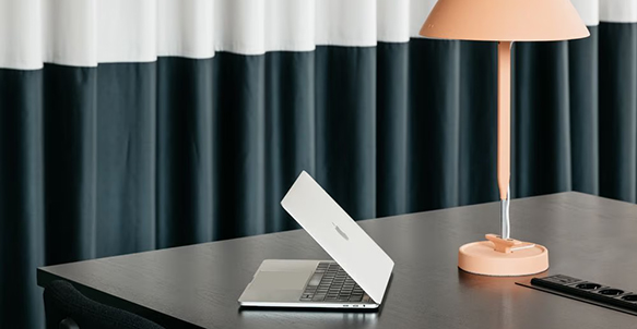 Detailaufnahme eines stilvollen Arbeitsplatzes mit Tischleuchte, dunklem Vorhang und modernen Accessoires.