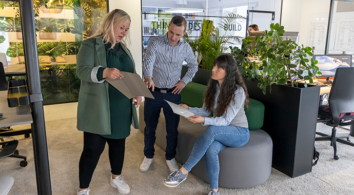 Drei Personen befinden sich in einer modernen Bürofläche und schauen gemeinsam ein Dokument an.